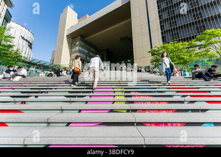 Die überfüllte Umekita Plaza mit den breiten Stufen, die an einem sonnigen Frühlingstag zum nördlichen zentralen Tor der Bahnhofsstadt Osaka hinaufsteigen. Stockfoto