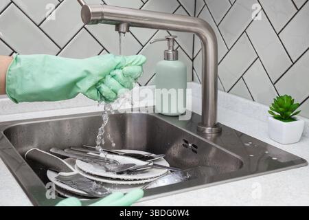 Hand in Gummihandschuhen den Schwamm unter fließendem Leitungswasser drücken oder abspülen, bevor Sie das Geschirr waschen, Wasser spritzen oder Hausarbeiten erledigen Stockfoto