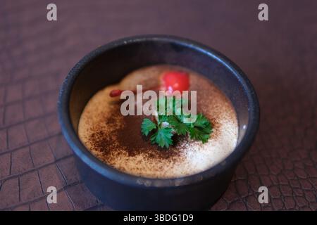 Perfekter, verzehrfertiger, hausgemachter Tiramisu-Kuchen mit frischer Minze. Tiramisu-Teil auf rosafarbener Platte auf weißem Marmorhintergrund. Köstliches Tiramisu ohne Backen. Hausgemachte Highland Tiramisu Creme Stockfoto