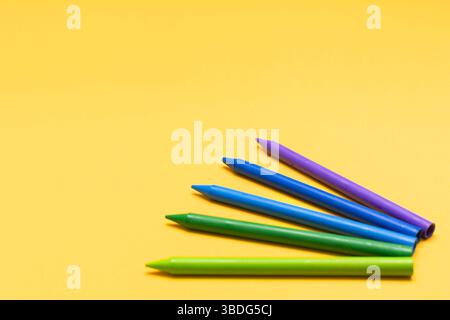 Fünf bunte Buntstifte in Fächerform auf hellgelbem Hintergrund. Minimalistische Komposition mit lebhaften Farben, geeignet für kreative und informative Zwecke Stockfoto