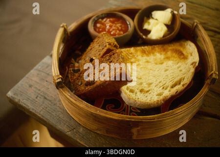 Rustikaler Brotkorb mit gerösteten Weißbrotscheiben, Fruchtbrotscheiben, Butter und Papaya-Marmelade Stockfoto