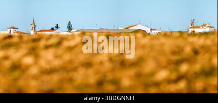Weiß getünchte Häuser von Carrión de los Céspedes erheben sich auf einem Hügel und überblicken tagsüber frisch gepflügtes Ackerland unter einem klaren blauen Himmel. Stockfoto