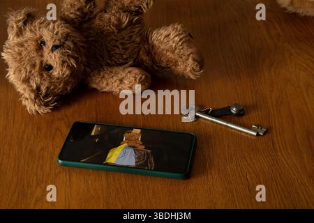Teddybär, alter Schlüssel und Smartphone mit Foto eines Mädchens mit Koffer und ukrainischer Flagge, Abschied und Verlassen des Hauses wegen des Krieges Stockfoto