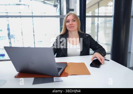 Selbstbewusste junge Frau, die an einem Laptop in einem modernen Coworking-Raum mit Tageslicht und Pflanzen arbeitet. Stockfoto