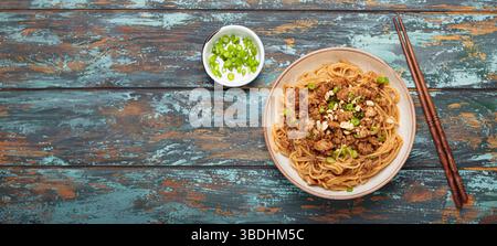 Dan Dan Dan Nudeln serviert mit Essstäbchen und grünen Zwiebeln von oben auf rustikalem Holztisch, traditionelles chinesisches Sichuan-Gericht Stockfoto