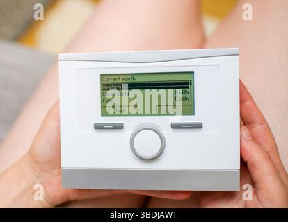 Eine Frau hält einen Gaskessel-Controller, der den aktuellen monatlichen Energieverbrauch anzeigt, wobei die Heizungs-, Strom- und Brennstoffverbrauchswerte auf dem Di angezeigt werden Stockfoto