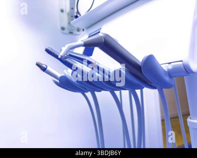 Nahaufnahme mehrerer Zahnhandstücke, die an einer Einheit in einer hell beleuchteten Zahnklinik befestigt sind, mit Schwerpunkt auf den metallischen Texturen und dem gekrümmten Inst Stockfoto