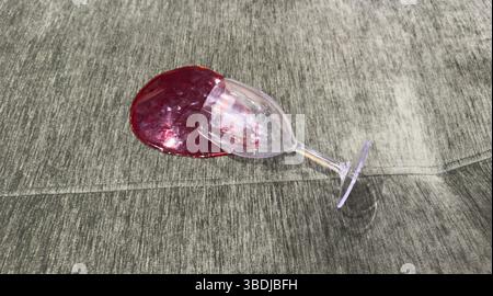 Ein Glas Rotwein ist auf ein grünes Stoffsofa gekippt und hat einen großen Fleck mit sichtbaren Spritzern und weichen Reflexen auf dem Polster erzeugt Stockfoto