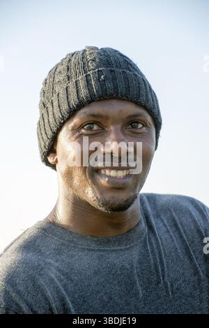 Ein Porträt eines lächelnden Afrikaners mit einem grauen T-Shirt und einem grauen Wollbock auf dem Kopf Stockfoto