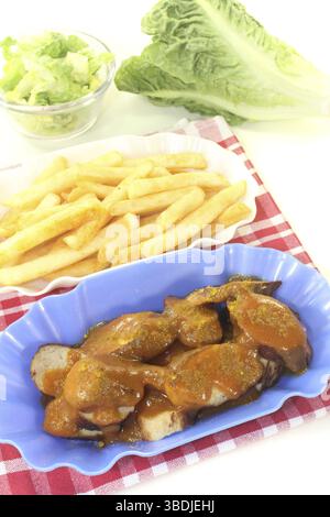 Currywurst mit Chips und Salat vor hellem Hintergrund Stockfoto