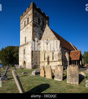 Frontalansicht einer historischen Kirche mit einem weiß getünchten Steinturm, flankiert von Feuersteingiebeln, mit einem rustikalen Holzzaun im Vordergrund. Stockfoto