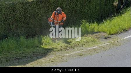 Ein stadtarbeiter Clearing am Straßenrand von Gras und Unkraut mit einem weed Eater Stockfoto