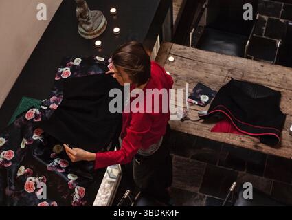 Draufsicht einer Designerin, die schwarzen Blumenstoff zum Nähen misst und vorbereitet. Das Konzept des Hobbynähens, Schneidens, Gestaltens, Handwerks Stockfoto