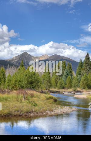 Der klare Fluss windet sich durch Kiefernwälder unter felsigen Berggipfeln Stockfoto