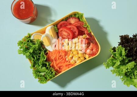 Frischer Sommersalat mit Garnelen, Mais, gekochtem Ei, Tomaten, Karotten, und Salat. On Yellow Bowl Top View, Konzept der gesunden Ernährung. Stockfoto