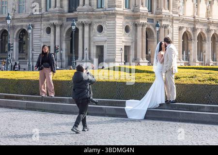 Braut und Bräutigam küssen und posieren für Hochzeitsfotograf vor dem Louvre Palace in Paris, Frankreich Stockfoto