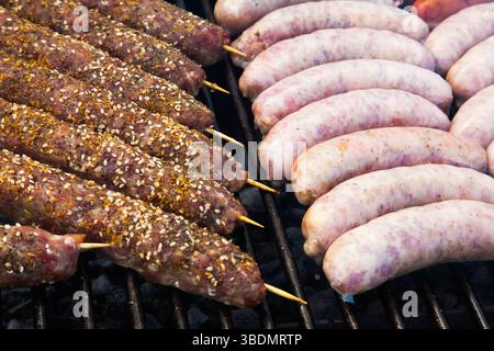 Würstchen und Hackfleisch auf Holzstäbchen werden auf dem Grill gekocht. Stockfoto