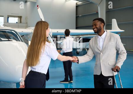 Eine Pilotin schüttelt mit Geschäftsmann im Flugzeughangar die Hand Stockfoto