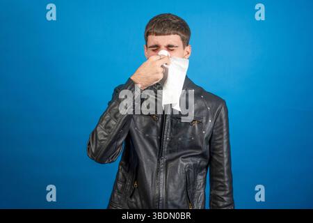 Studio-Aufnahme eines jungen Mannes, der sich mit einem Gewebe die Nase bläst, an Rhinitis oder Erkältung leidet Stockfoto