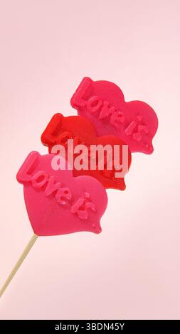 Vertikales Banner zum Valentinstag. Drei rote Herzlutscher auf rosa Hintergrund. Süße Liebe. Stockfoto