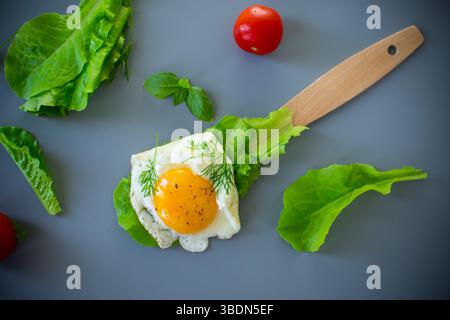 Nahaufnahme von leckerem Ei mit Salatblättern in der Küche, auf grauem Hintergrund. Stockfoto