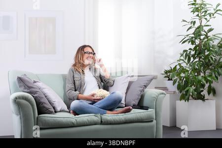Eine Frau mit einer intelligenten Brille, die Popcorn hält und ihre Brille berührt, als ob sie mit einem virtuellen Display interagiert. Blick in den Weltraum mit digitalem und digitalem Stockfoto