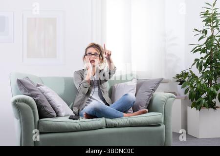Staunte junge Frau, die eine intelligente Brille mit Smartphone neben sich trägt. Sie berührte den Bildschirm und blickt nach vorne, als ob sie mit digitalen Inhalten an einem Computer interagieren würde Stockfoto