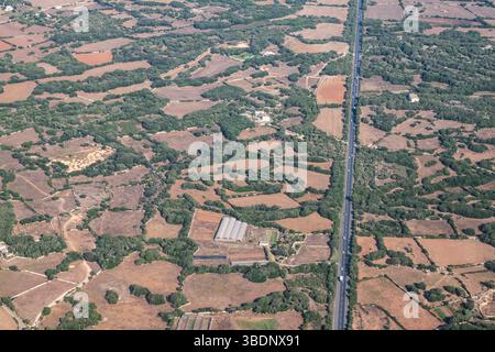 Gerade Straße mit Autos durch die landwirtschaftliche Landschaft der spanischen Insel Menorca. Stockfoto