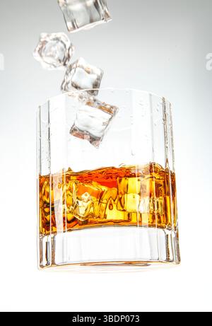 Held-Aufnahme eines Whiskyglases mit spritzenden Eiswürfeln, die die satte bernsteinfarbene Flüssigkeit und die dynamische Bewegung zeigen. Stockfoto