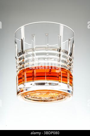 Held-Aufnahme eines raffinierten Glases Whiskey mit Eis auf den Felsen, das die reiche bernsteinfarbene Flüssigkeit zeigt. Stockfoto