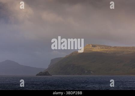 Goldenes Sonnenlicht fängt einen Bergrücken über dem Meer auf der Isle of Skye, Schottland, unter brütenden Sturmwolken. Stockfoto