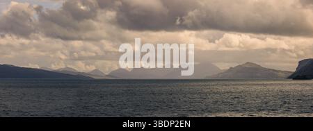 Blick über das Meer auf die Cuillin-Bergkette auf der Isle of Skye, Schottland, mit dramatischen Wolken und Küstenlicht. Stockfoto
