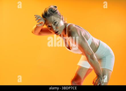 Schöne reife sportliche Frau, die Sportswear trägt, beim Training - schwitzige reife Sportlerin, die nach einem intensiven Workout inne hält und sich die Stirn mit dem Witz abwischt Stockfoto