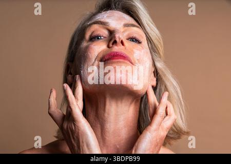 Schönheitsprofil der schönen Reifen Frau, Konzepte über Kosmetik, Hautpflege und Wellness. Reife blonde Frau massiert sanft Feuchtigkeitscreme auf Stockfoto