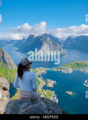 Ein Wanderer genießt einen ruhigen Moment auf einem Berg in Norwegen, mit Blick auf atemberaubende Fjorde und lebhaftes Dorfleben. Reinebringen Lofoten Norwegen Stockfoto