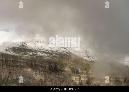 Hoch aufragende Klippen mit Blick auf einen dichten Wald und schneebedeckte Gipfel schaffen einen atemberaubenden Kontrast aus Texturen und Farben. Stockfoto