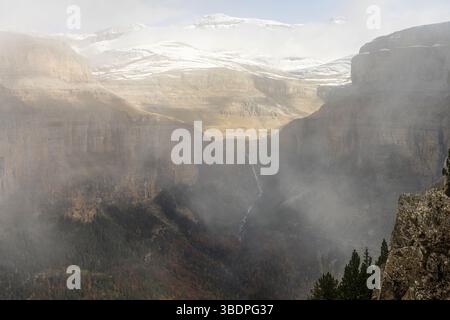 Hoch aufragende Klippen mit Blick auf einen dichten Wald und schneebedeckte Gipfel schaffen einen atemberaubenden Kontrast aus Texturen und Farben. Stockfoto