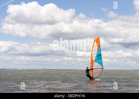 Swale Sittingbourne, Großbritannien. Mai 2025. Wetter in Großbritannien: Sonniger Sonntag entlang der Küste von Kent: Windsurfer ziehen mit einer sanften Brise in der Luft auf einem Segelbrett ins Wasser, während Strandgäste sich in der warmen Nachmittagssonne sonnen. Eine lebendige Mischung aus Entspannung und Abenteuer, während die Küstenszene zum Leben erweckt wird Credit: xiu bao/Alamy Live News Stockfoto