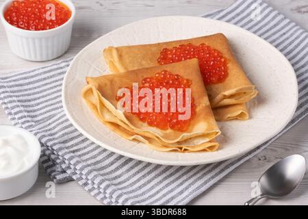 Köstliche Crepes mit rotem Kaviar serviert auf einem gemütlichen Tisch bei Tageslicht Stockfoto