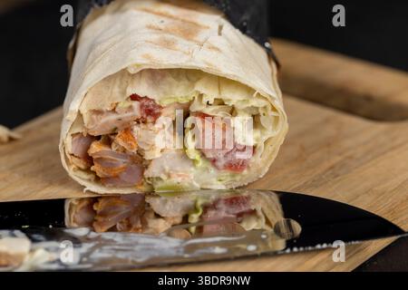 Shawarma aus dünner Weizentortilla mit Fleisch mit Tomaten und Sauce, Fast Food Shawarma aus verschiedenen Zutaten in Folie verpackt Stockfoto