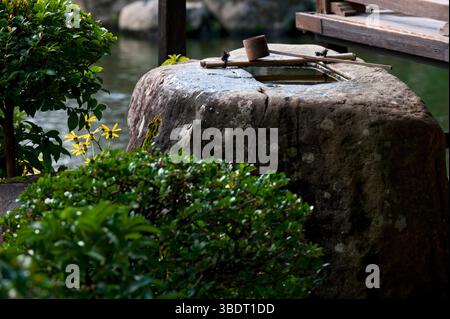 'Tsukubai' (Steinwasserbecken) mit einem 'Hishaku' (Bambusschöpfe) neben einem japanischen Teehaus im Tenshaen Zen Landschaftsgarten, Uwajima, Ehime, Japan. Stockfoto
