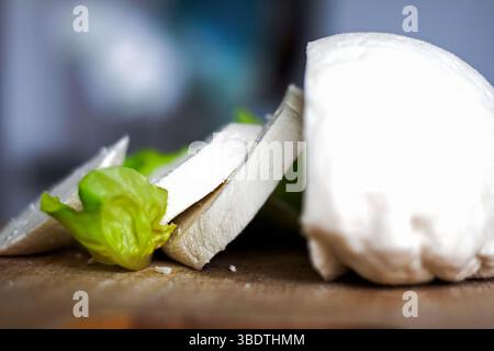 Foto: Frischer hausgemachter Käse, in dicke Scheiben geschnitten, Seitenansicht mit Salat dekoriert. Eine Art Hüttenkäse, Quark-Produkte, die traditionell handgemacht werden Stockfoto