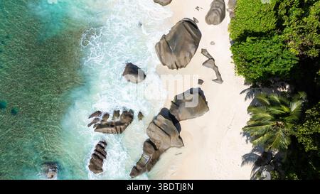 Felsbrocken verstreut über einen weißen Sandstrand mit türkisfarbenem Wasser, das sanft über die Küste plätschert. Seychellen, Mahe. Carana Beach. Stockfoto