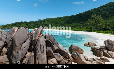 Felsiger Felsvorsprung mit smaragdgrünem Wasser und dichtem Laub, neben einem weißen Sandstrand. Anse Cocos. Seychellen, La Digue. Stockfoto