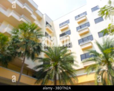 Abstrakter, verschwommener zeitgenössischer Stil eines gelben Hotelgebäudes mit tropischen Palmen, Sommerferien, Reiseunterkunft im Hintergrund. Backgr Stockfoto