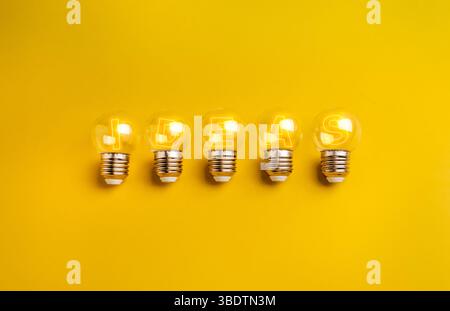 Fünf leuchtende kleine, klare Glühlampen mit leuchtendem Text „IDEEN“ im Inneren, isoliert auf gelbem Hintergrund. Intelligentes Business-Team, Innovationstechnologie, Crea Stockfoto