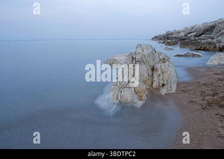 Sanfte Wellen sprudeln über Felsen an einem ruhigen, bedeckten Strand Stockfoto