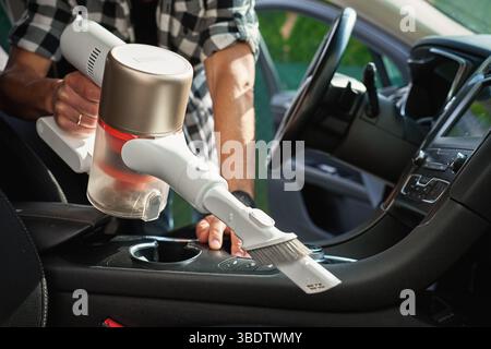 Man saugt schmutziges Fahrzeuginnere mit einem kabellosen Handstaubsauger ab. Autobesitzer kümmern sich um Fahrzeug, Sitzpolster und Innenraum reinigen. Vehi Stockfoto