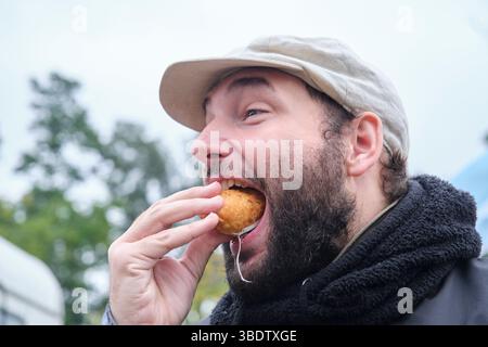Junger Mann genießt im Freien frisch zubereitete Empanada aus argentinischem Schinken und Käse. Stockfoto