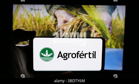 In dieser Abbildung hält eine Person ein Handy mit dem Logo der paraguayischen Düngemittelfirma Agrofertil S.A. auf dem Bildschirm vor der Webseite. Stockfoto
